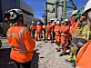 Arbeidere i oransje vernetøy står samlet til sikkerhetsmøte på byggeplass.