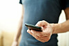 En mann står med en mobiltelefon i sin ene hånd. Han ser ut til å sjekke innholdet på skjermen.