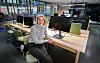 Kvinne sitter ved skrivebord i et moderne åpent kontorlandskap med dataskjermer og arbeidsplasser.