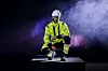 Person i refleksklær og hjelm sitter på en plattform i røykfylt, mørk setting med lilla lys.