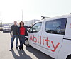 To personer som står ved siden av en tjenestebil for selskapet Ability.