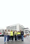 Gruppebilde av renholdsledere ved Stavanger Universitetssjukehus. De står på en parkeringsplass med deler av sykehuset på Ullandhaug i bakgrunnen.