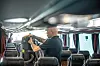 Mann som setter et batteri inn i en ryggbåren støvsuger, for å støvsuge i en buss.