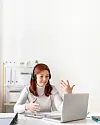 Ung kvinne som sitter ved et skrivebord. Foran seg har hun en bærbar PC og er i en videosamtale.