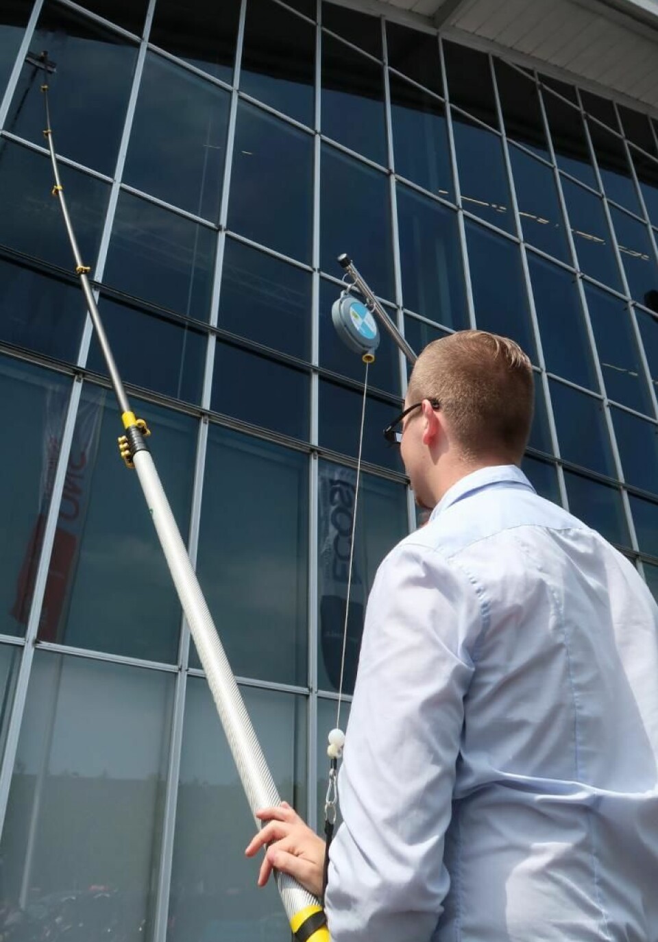 Bilde av en person som vasker vinduer i høyden ved hjelp av et rentvannssystem og teleskopstenger.