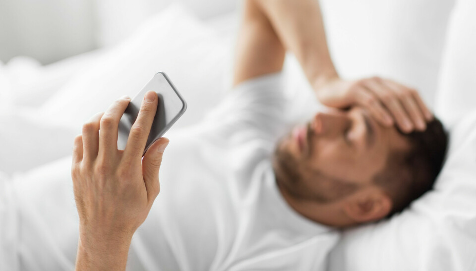 Syk mann som ligger i senga, med mobiltelefon