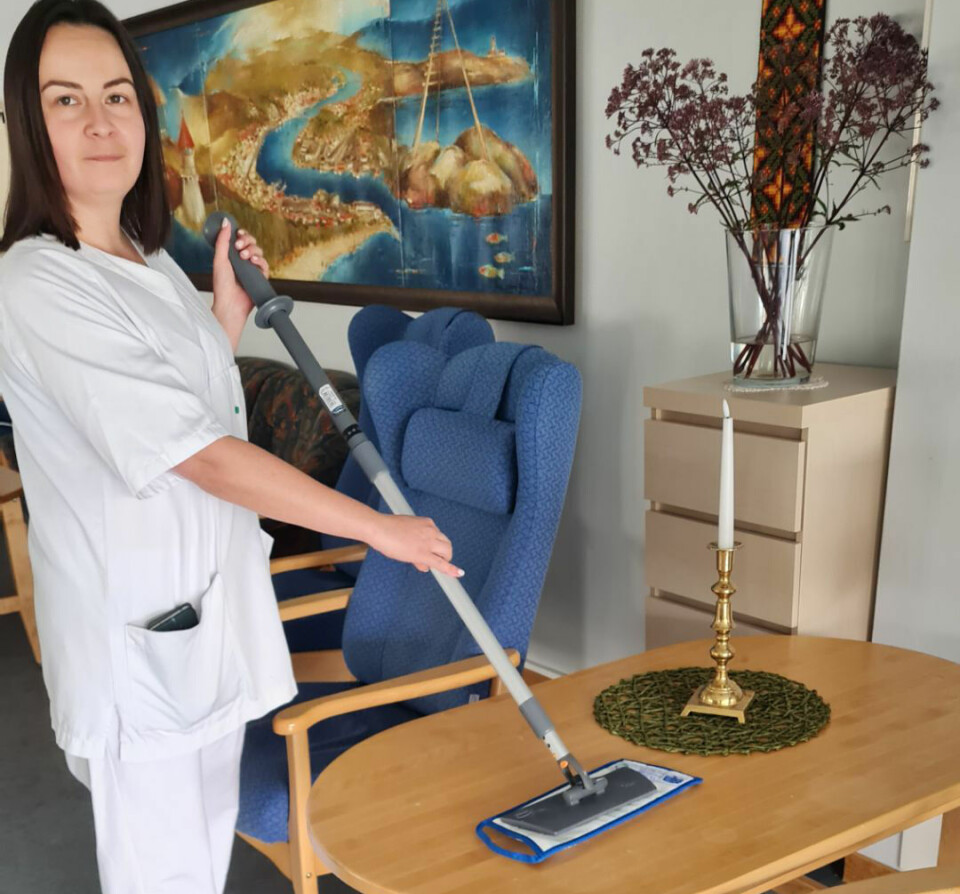 Monika Miron tørker støv av et lavt bord, ved hjelp av en tavlemopp