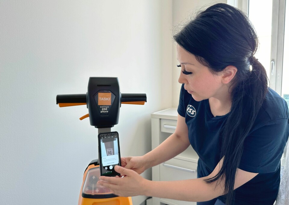 Kvinne scanner QR-kode på renholdsmaskin ved hjelp av en mobiltelefon